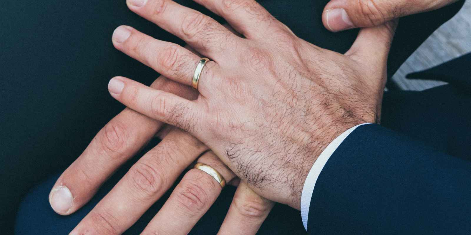 Photo of one hand on top of another, both wearing wedding rings