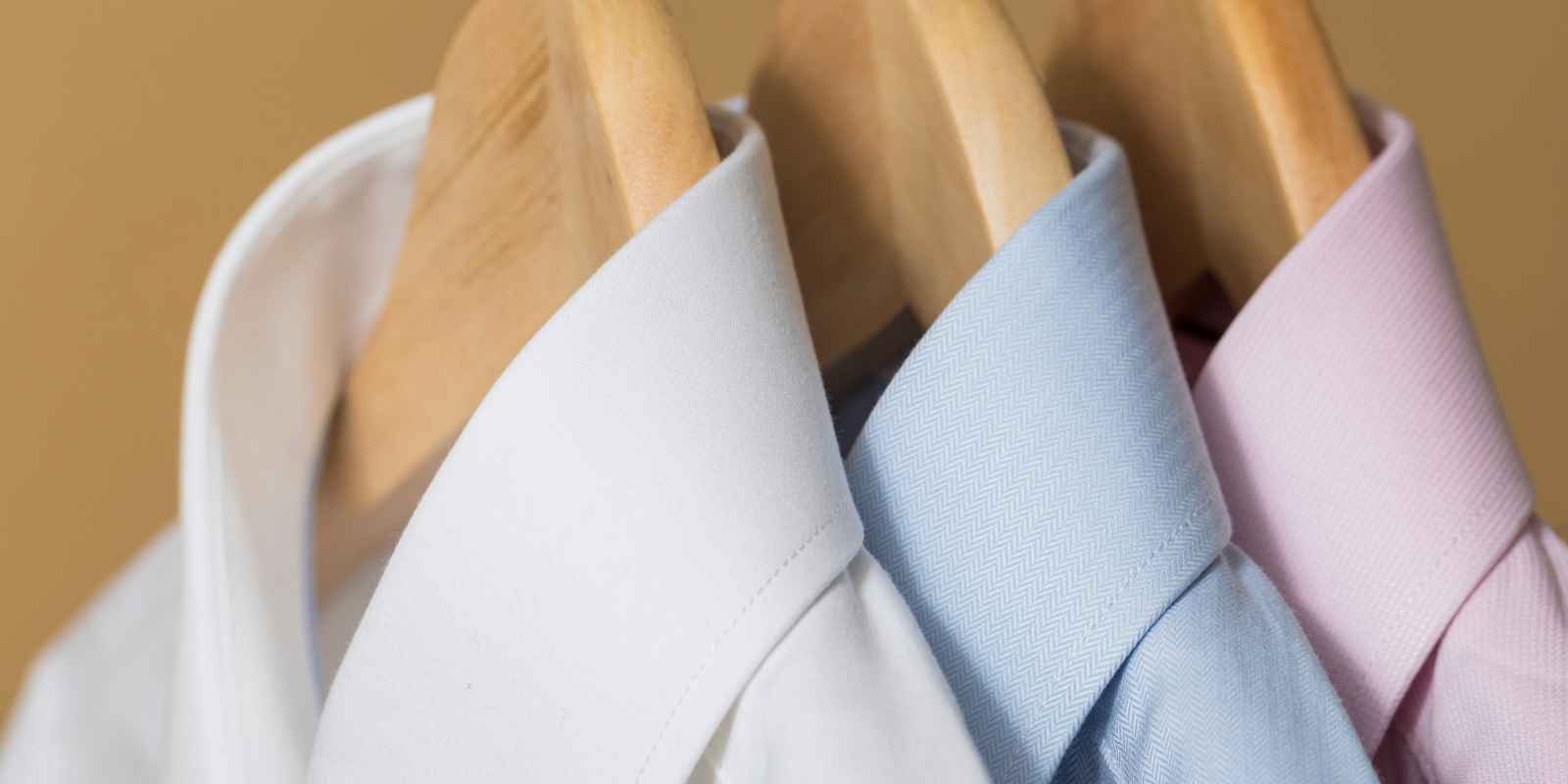 Up close photo of a white, light blue and light pink collard shirts on wood hangers.