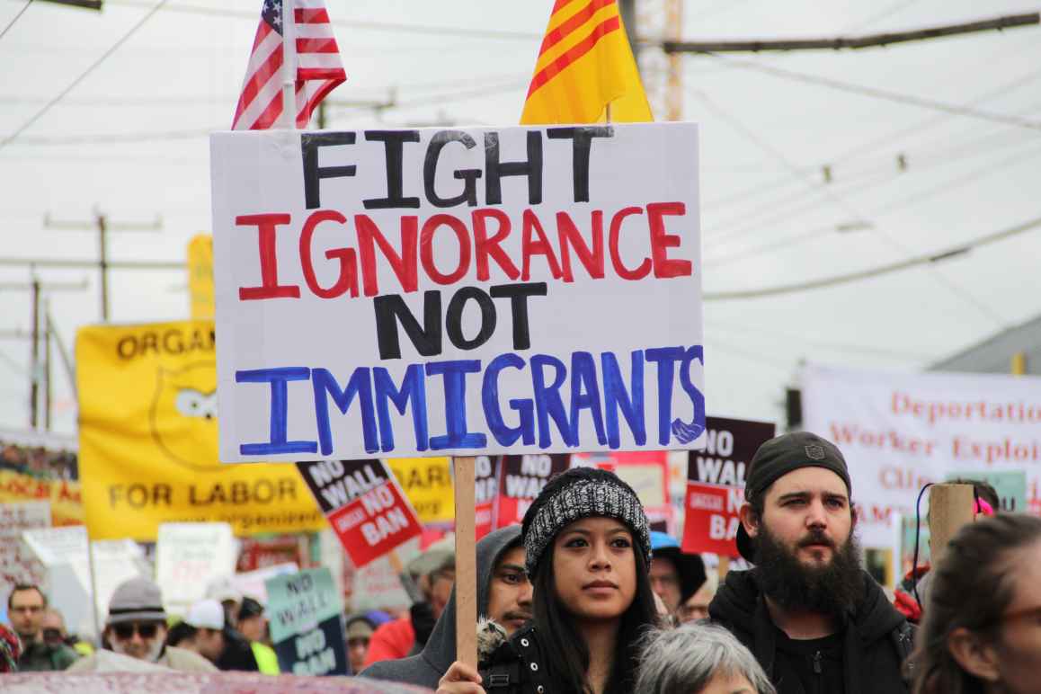 person holding protest sign saying "fight ignorance not immigrants" 