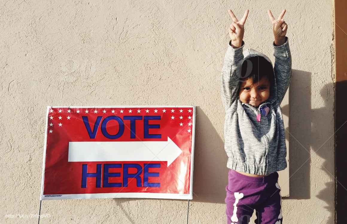 child next to a vote here sign